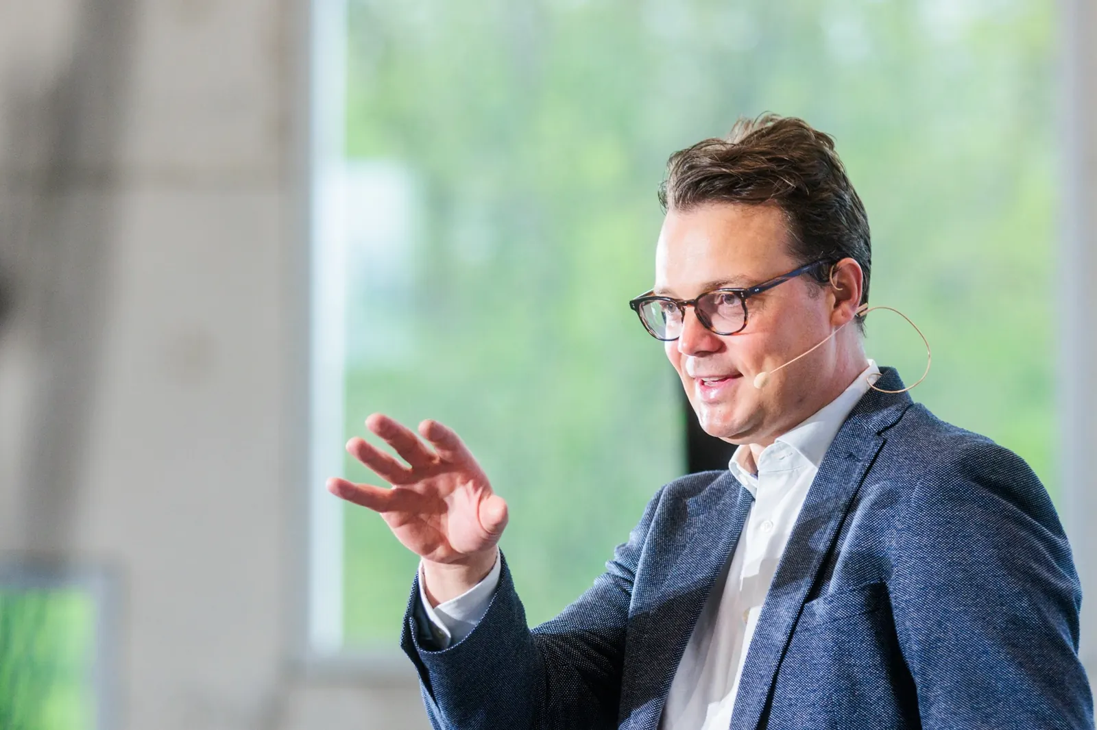 Jens Issel mit erhobener Hand im Gespräch vor großen Fenstern