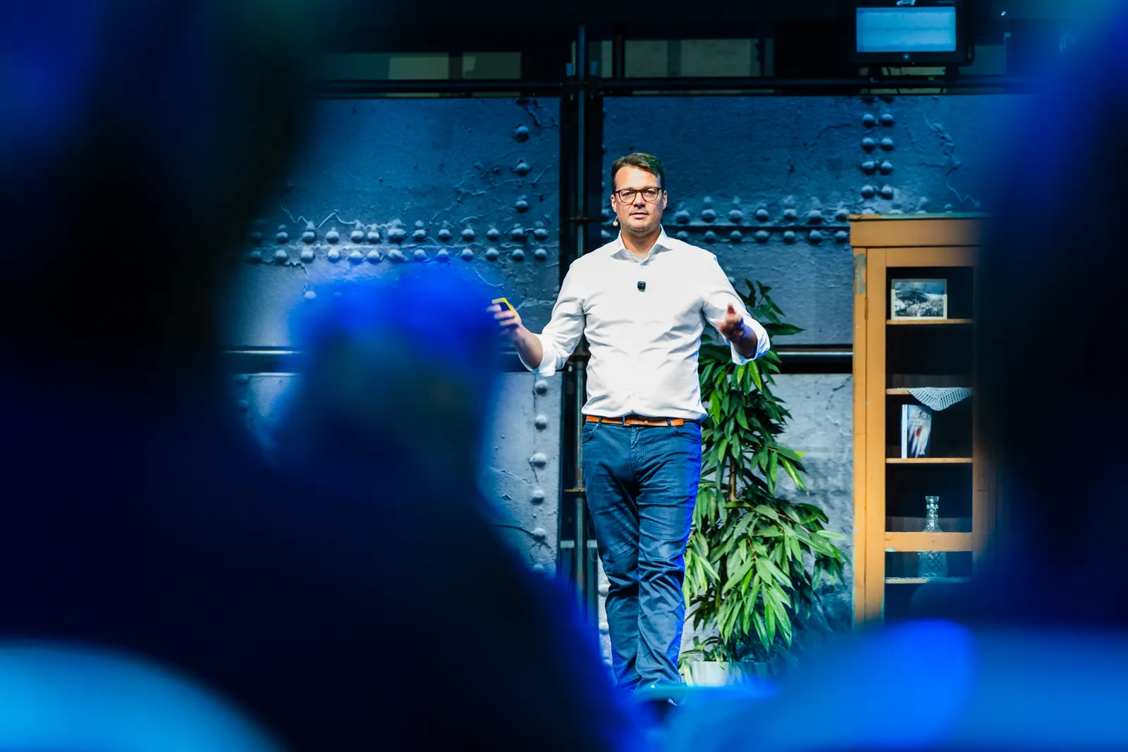 Jens Issel steht in blauem Bühnenlicht, im Vordergrund unscharf das Publikum
